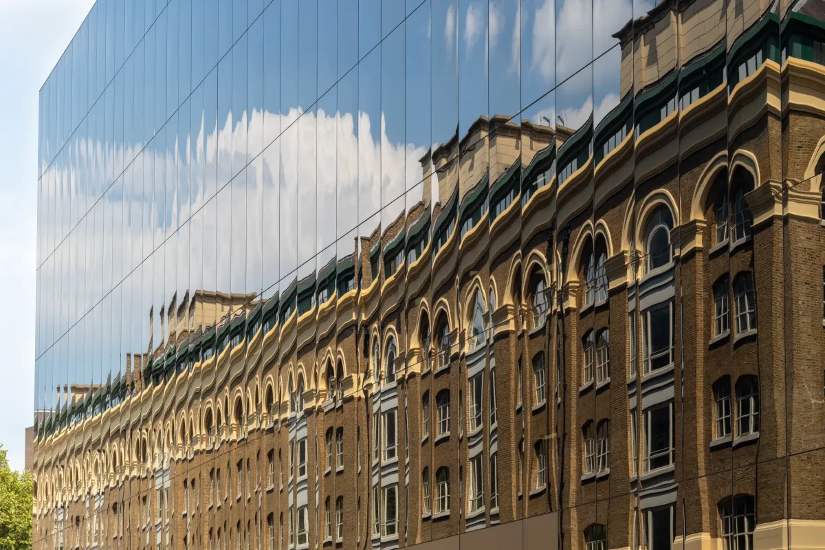 old office building reflected in the facade of new glass building