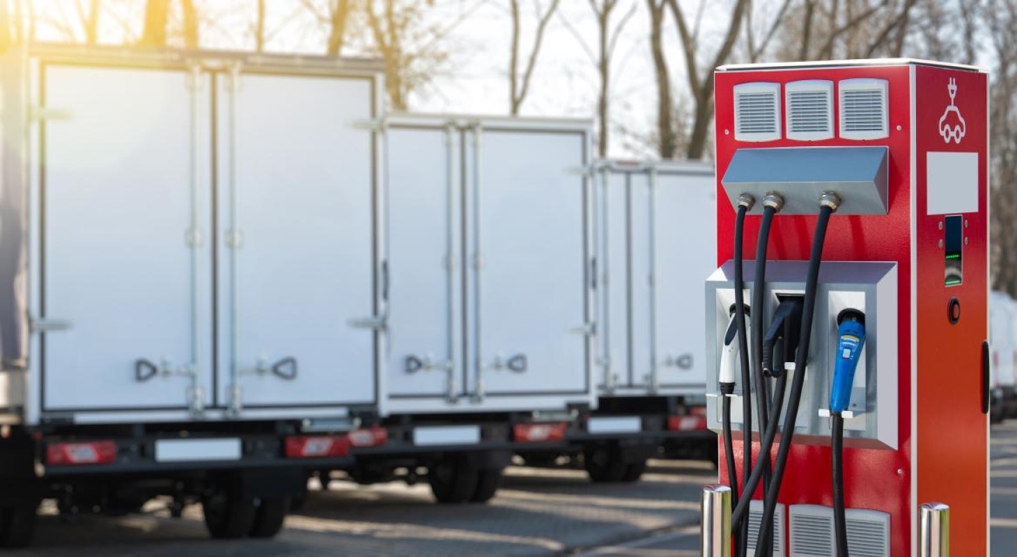 row of electric box delivery trucks behind red charging station