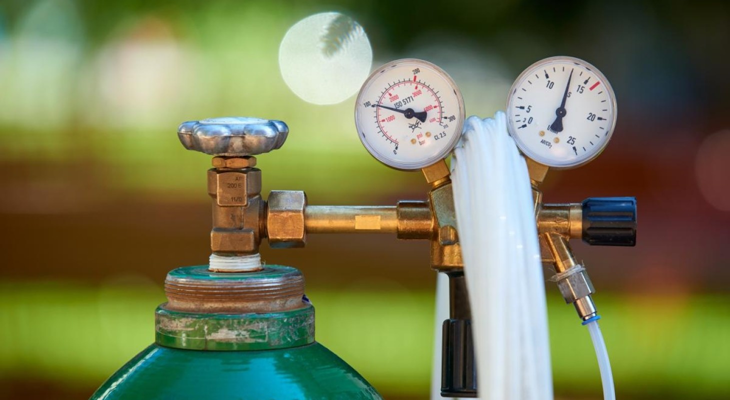 green gas tank with clear tubing and two pressure gauges