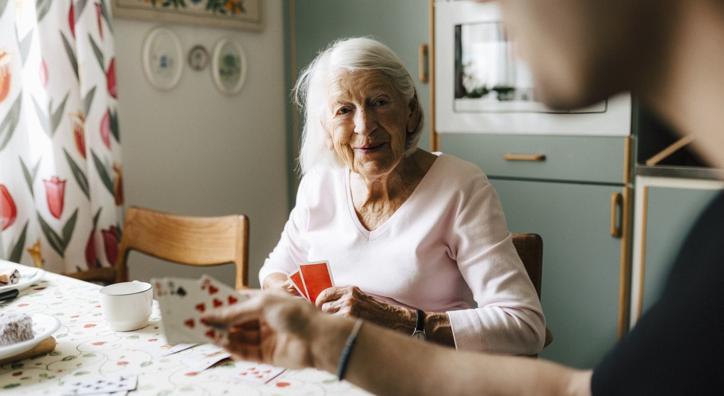 elderly woman playing cards with male nurse at dining table