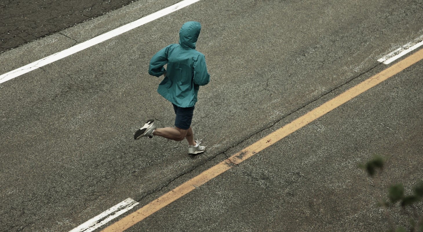 main in teal rain jacket running on divided road