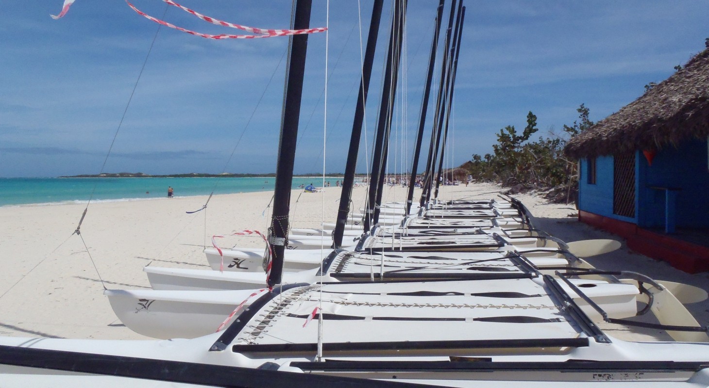 hobie cat sailboats without sails lined up on white beach