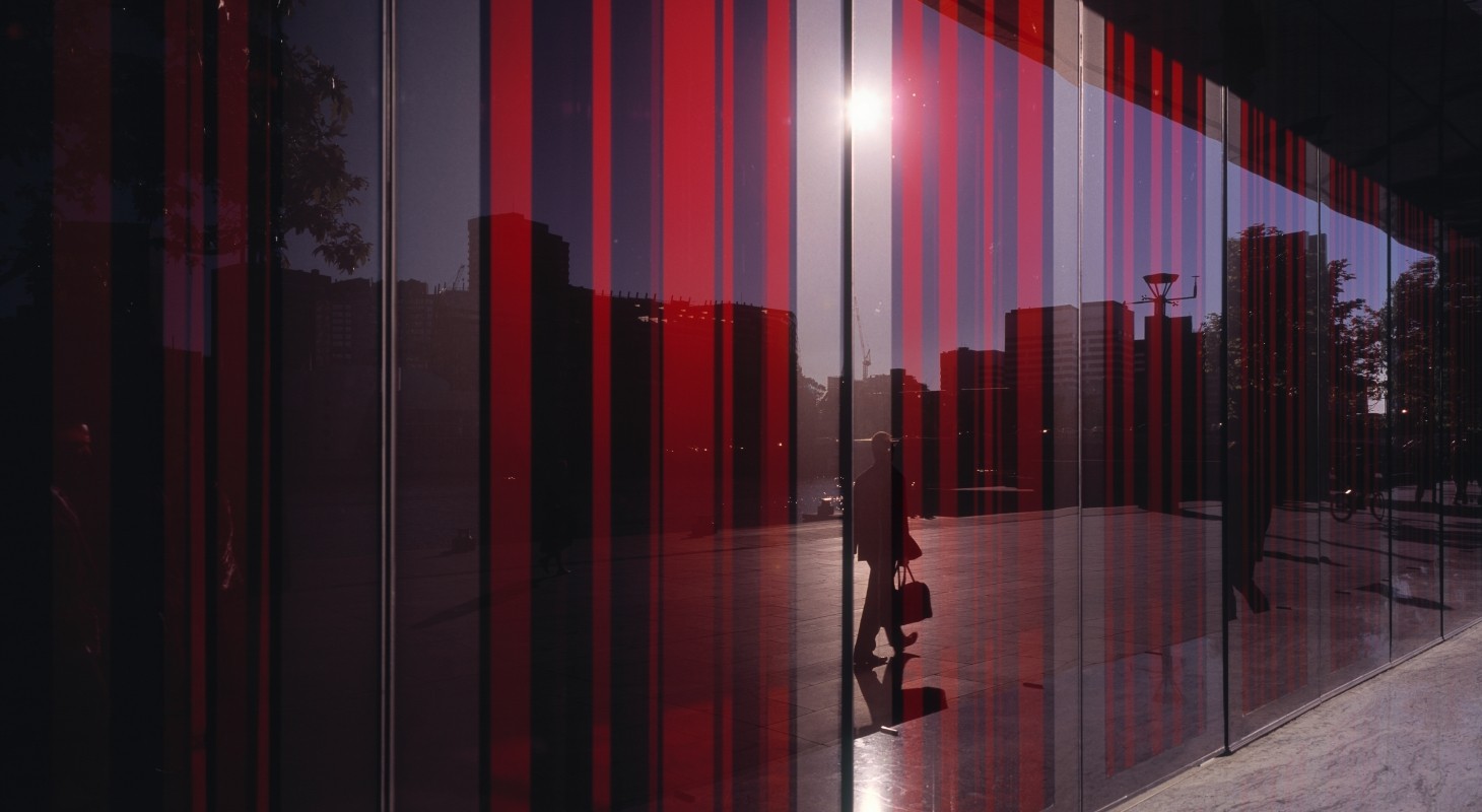 glass facade with red shades reflecting man on sidewalk with briefcase