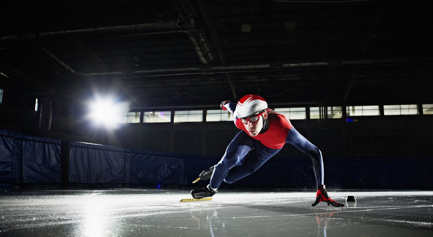 short track speed skater in dark rink with red and blue  uniform