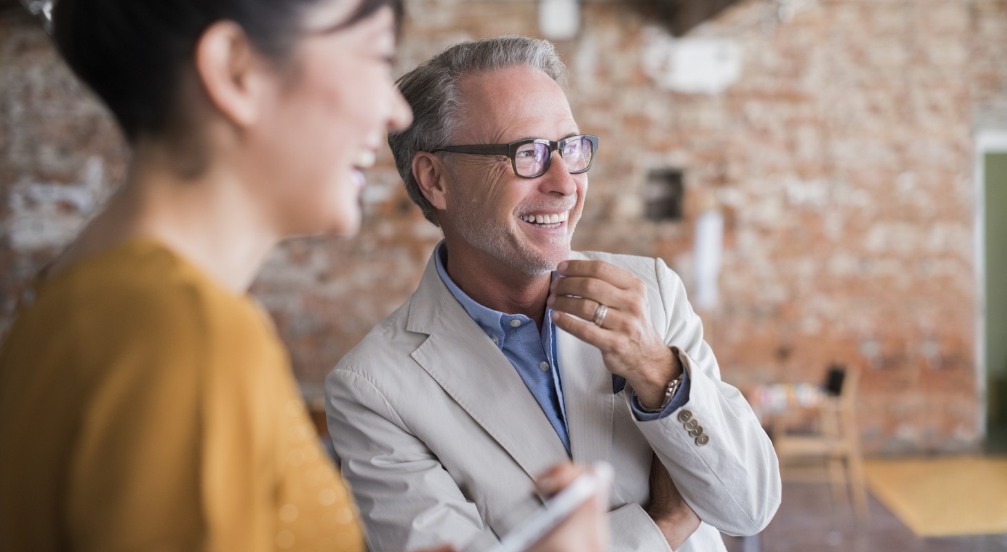 man in suit jacket with gray hair laughing with dark haired female executive