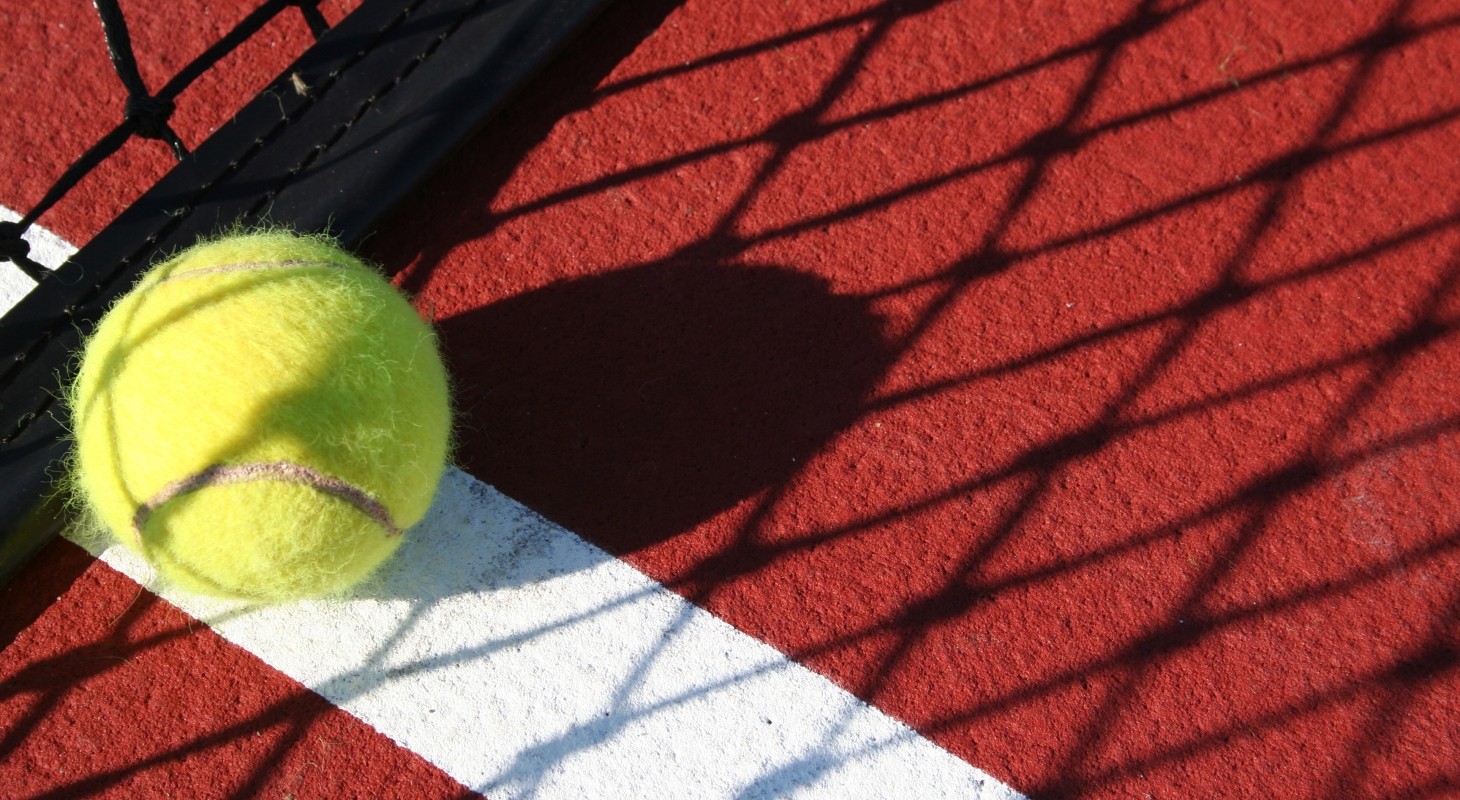 close up of yellow tennis ball on red court in shadow of net