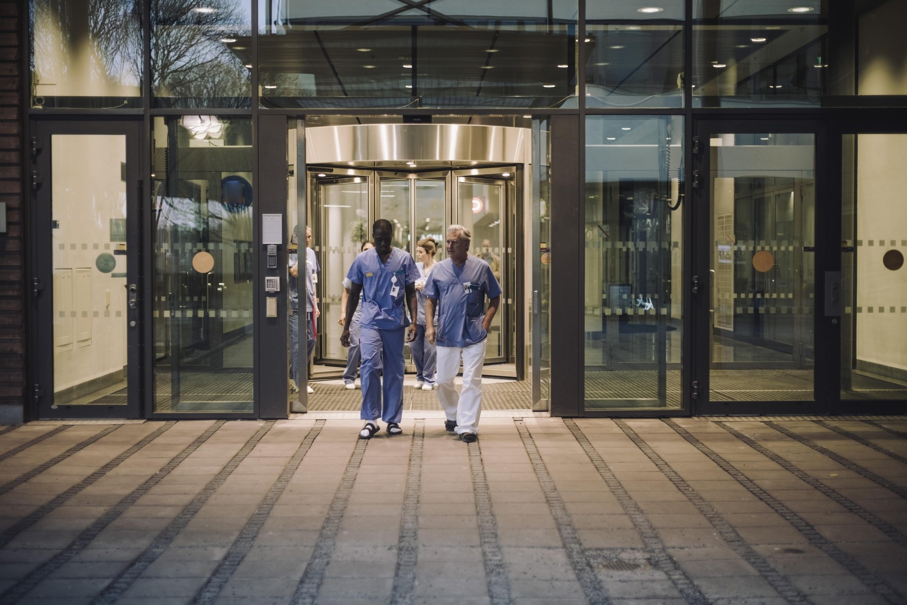 multiracial male doctors in scrubs leaving hospital at night