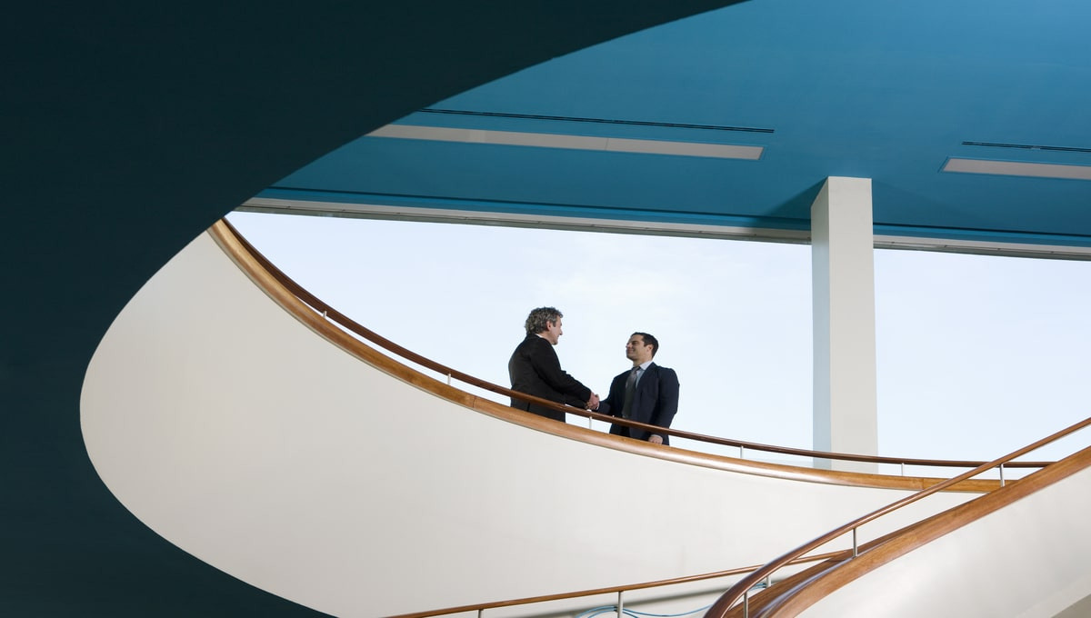 two businessman standing on balcony shaking hands