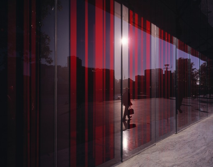 glass facade with red shades reflecting man on sidewalk with briefcase