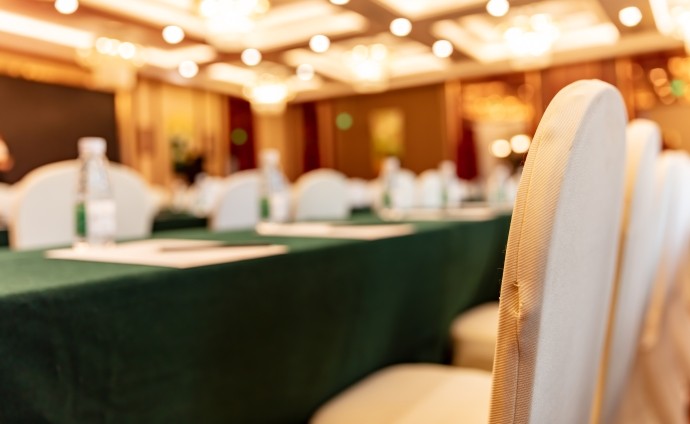 blurred view of large empty conference room with gold chairs and green tablecloths