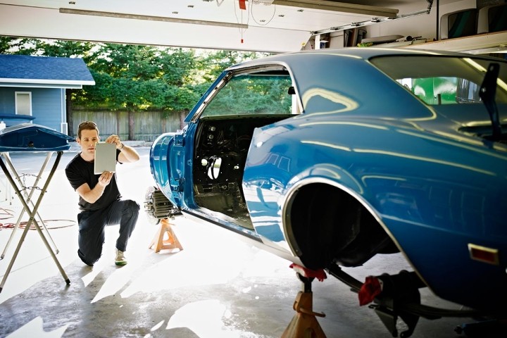 man working on blue classic car in a garage