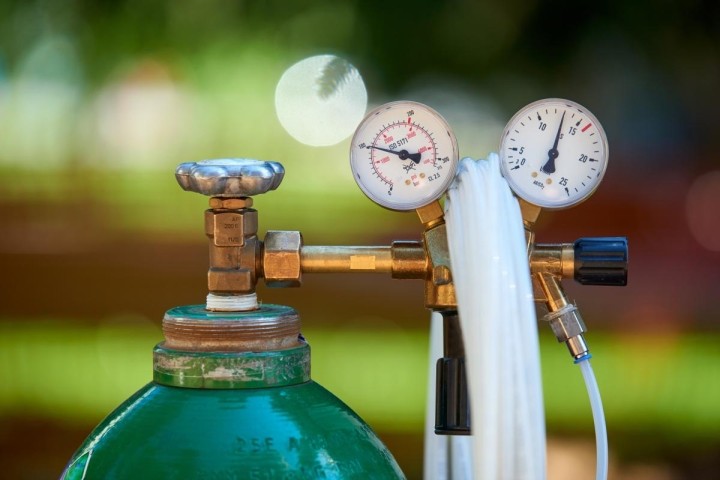 green gas tank with clear tubing and two pressure gauges