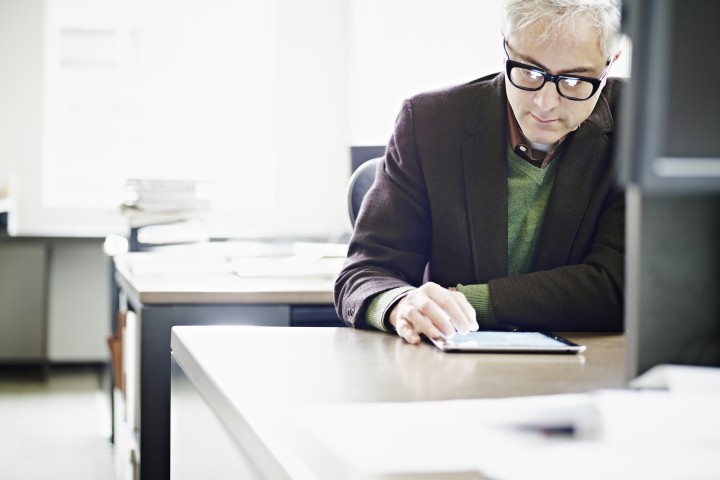 man with graying hair and glasses in suit jacked checking ipad