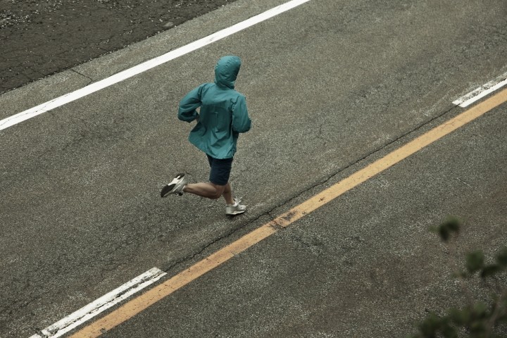main in teal rain jacket running on divided road
