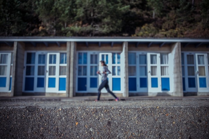 blurred focus of female runner on beach in front of low condos with blue doors