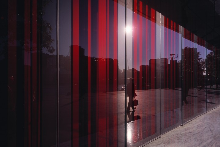 glass facade with red shades reflecting man on sidewalk with briefcase