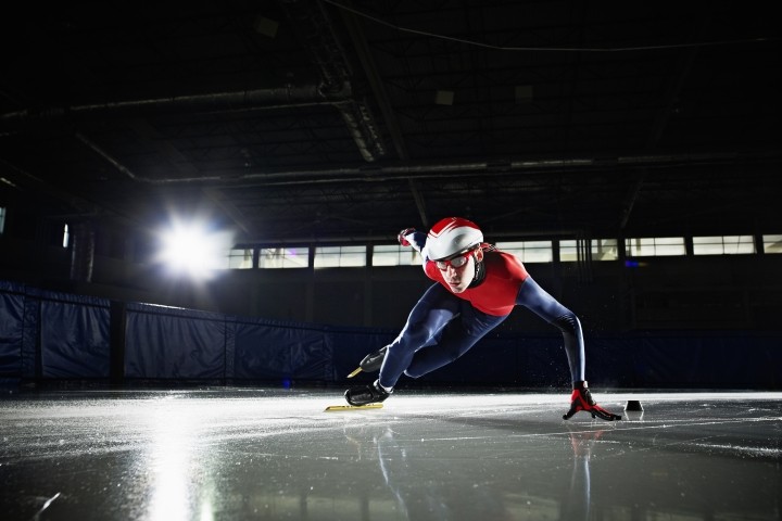 short track speed skater in dark rink with red and blue  uniform
