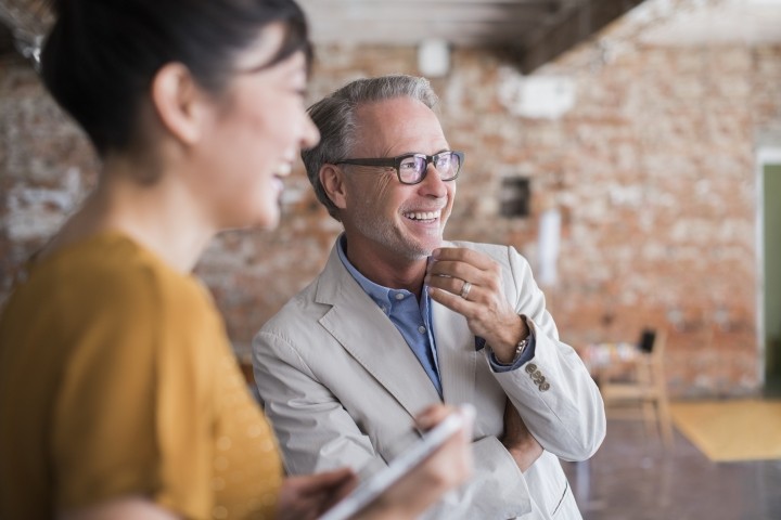 man in suit jacket with gray hair laughing with dark haired female executive