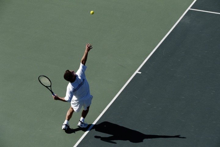 male tennis player serving on dark gray and green court