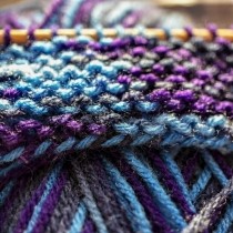 purple blue and gray yarns woven on knitting needle