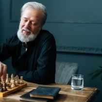 Portrait of happy bearded mature male performing move with pawn piece on wooden chessboard