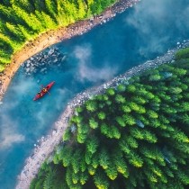 aerial view of red kayak on blue river between green forests 