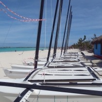 hobie cat sailboats without sails lined up on white beach