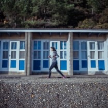 blurred focus of female runner on beach in front of low condos with blue doors